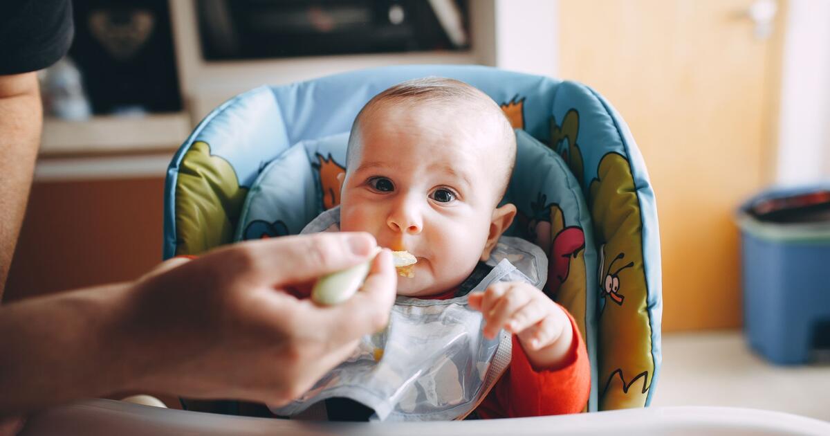baby eating first solid food spoon high chair