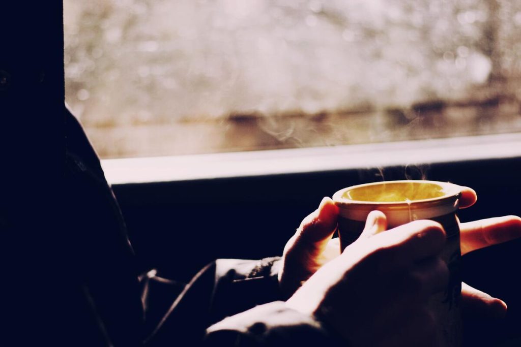 hand holding a cup of tea near a window, calm atmosphere, no face visible