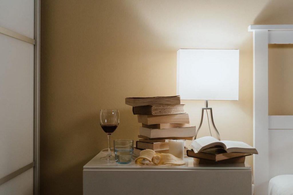 smartphone face down on nightstand next to a book and reading lamp
