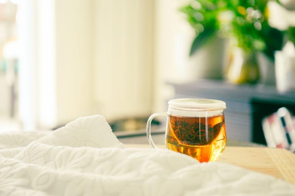 cup of herbal tea next to a heating pad on a cozy blanket, no people