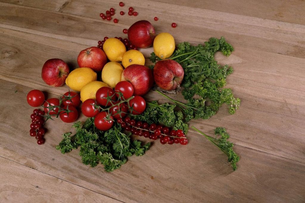 fresh fruits and leafy green vegetables arranged on a wooden kitchen table, no people