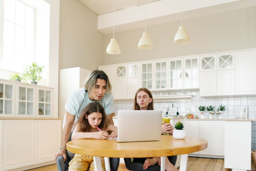 parent and teenager sitting at kitchen table with laptop, reading health information together, no visible faces