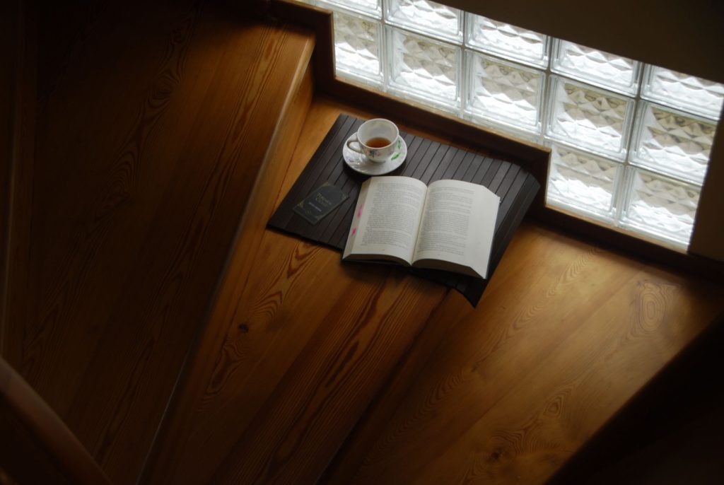 open book, reading glasses and a cup of tea on a wooden desk, warm natural light, no people