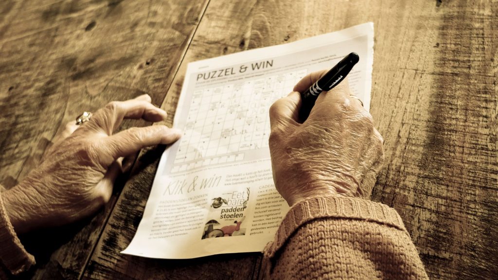 woman doing a crossword puzzle at a wooden table with coffee, cozy home setting, no face visible
